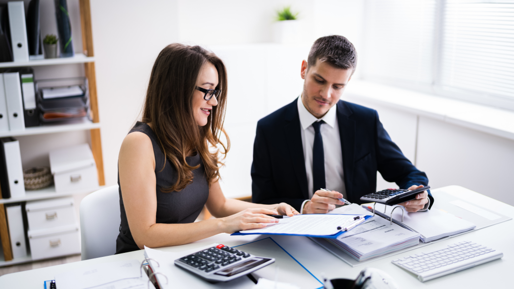 Two finance professionals discussing business loan options with calculators and documentation in a modern office.