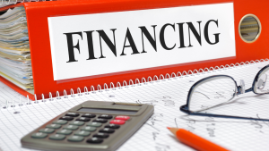 Close-up of a red binder labeled "FINANCING" with a calculator and eyeglasses on financial paperwork.