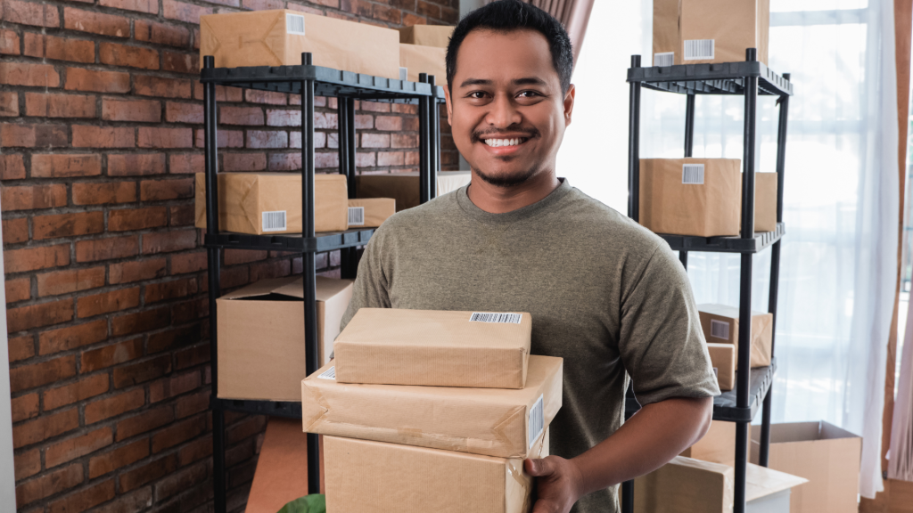 A small business owner smiles while packaging orders in a warehouse, representing proactive financial management and avoiding funding mistakes that could impact personal credit.