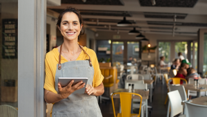 A proud small business restaurant owner smiles while holding a tablet, reflecting strong financial choices that protect her personal credit and business future.