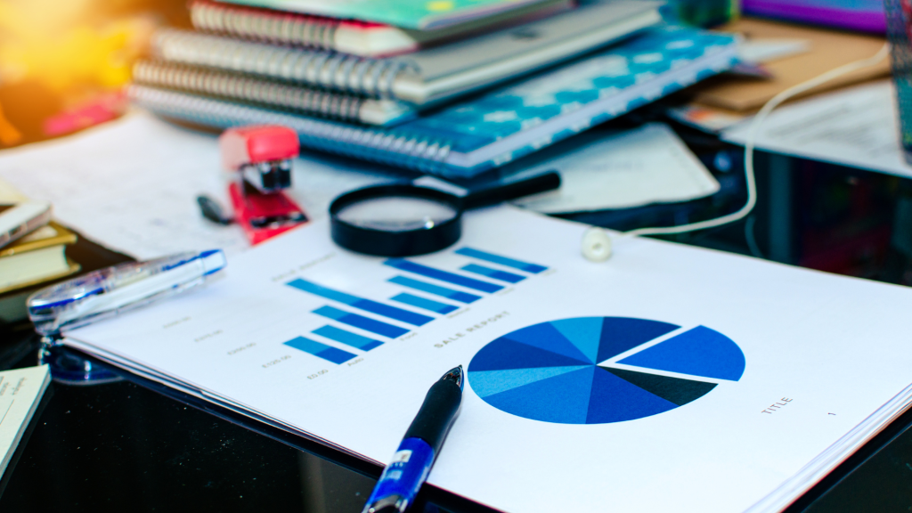 Business sales report with bar chart and pie chart on a cluttered desk, representing Equipment Financing plan and funding analysis.