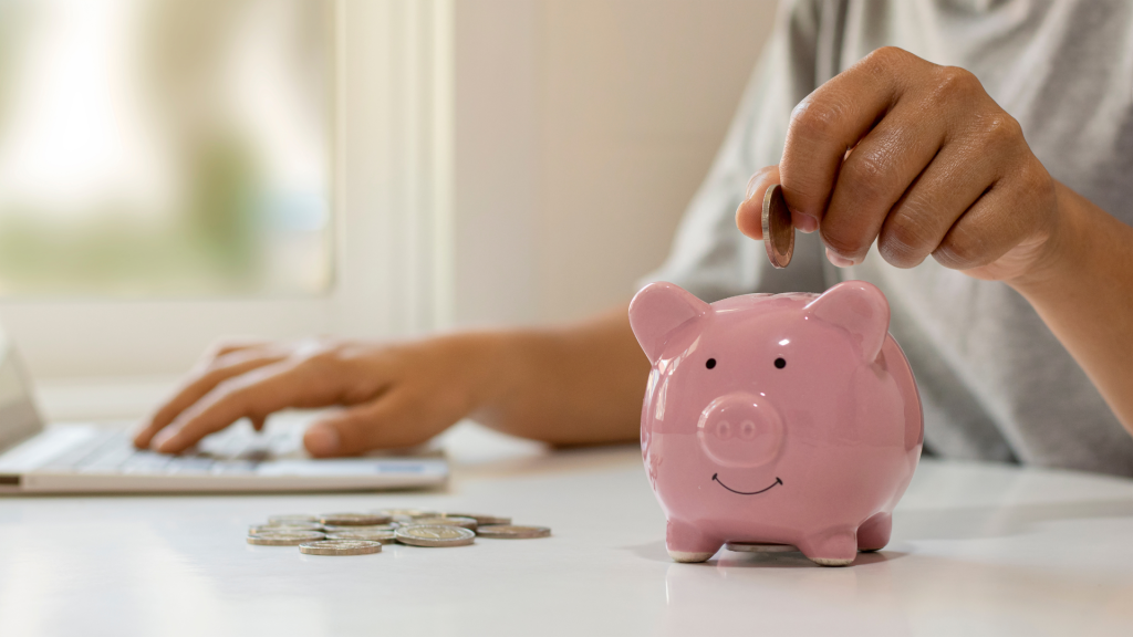 Business owner saving coins in a pink piggy bank while working on a laptop, symbolizing fast and smart funding decisions Avoid the bank.