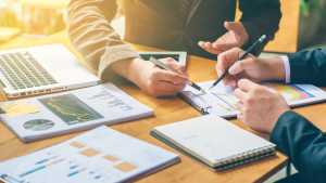 Hands of two professionals analyzing a success scan report with financial charts and graphs.